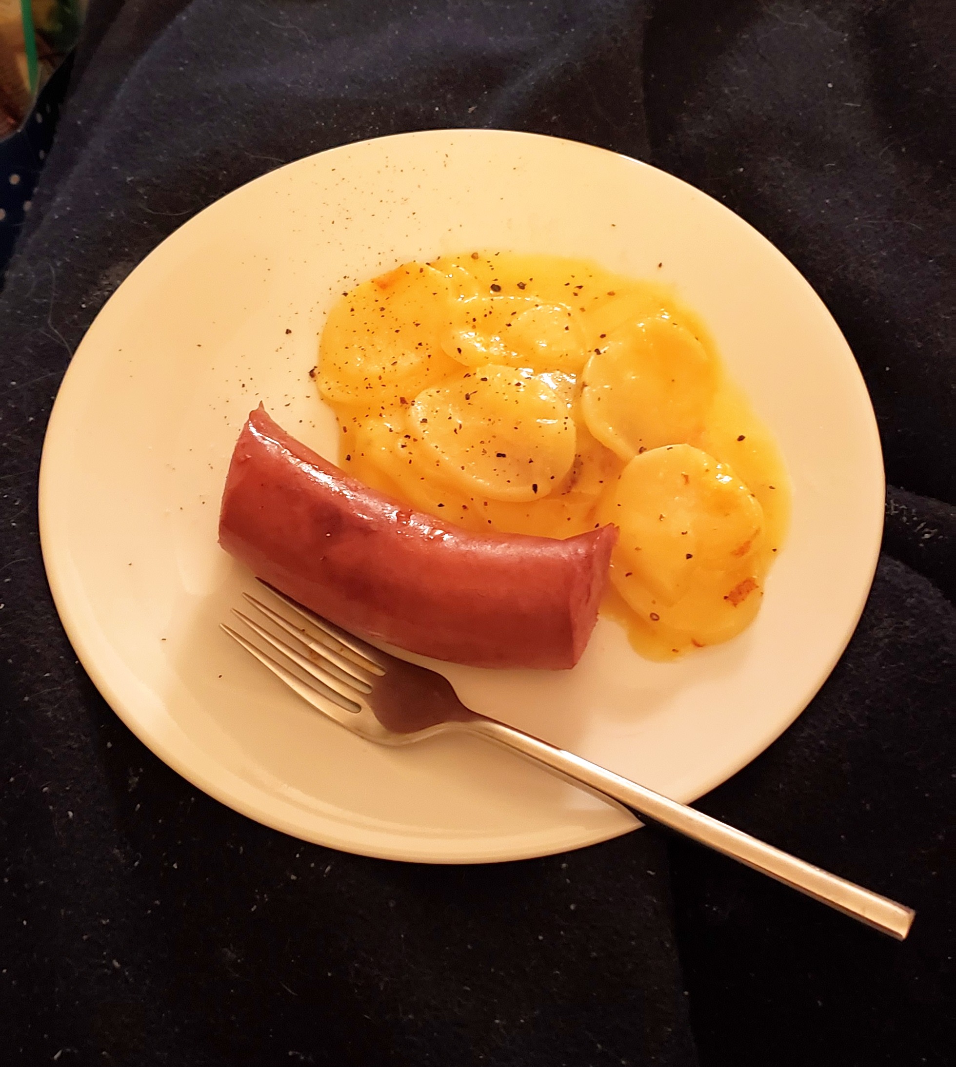 A white plate with a piece of kielbasa and a side of cheesy potatoes 