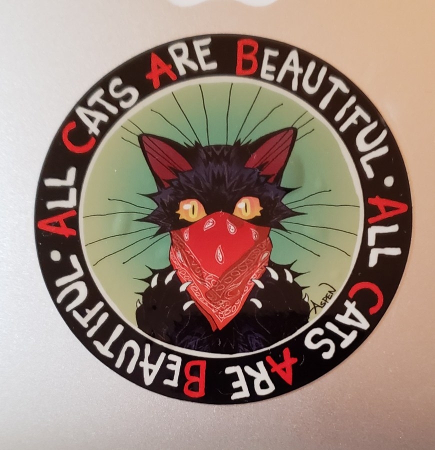 Black cat with a red bandana mask, with the words All Cats Are Beautiful