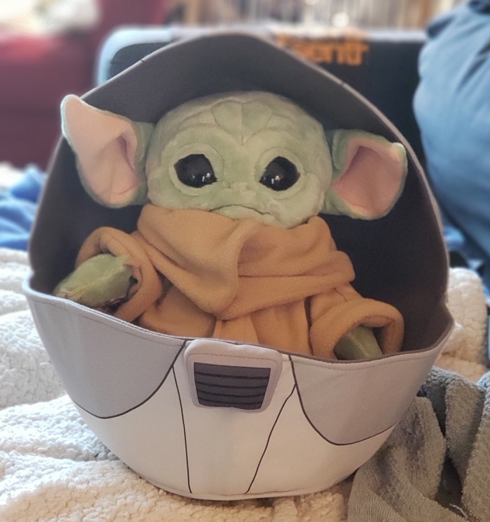 A Baby Yoda plush, in a space pram
