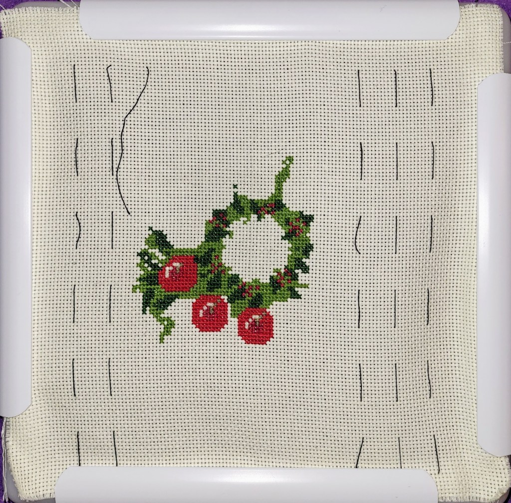 Work in Progress of Christmas Wreath cross stitch - center ring of greens done, with 3 apples 