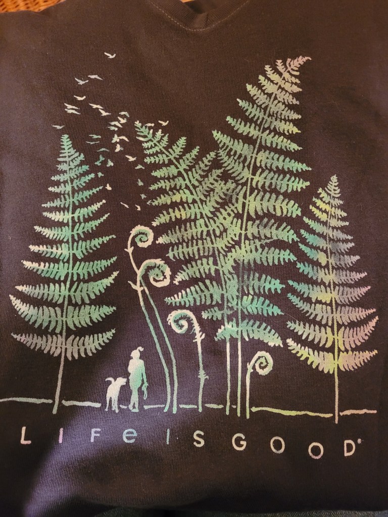 A black shirt with a "forest" of fern leaves and the silhouette of a girl and a dog