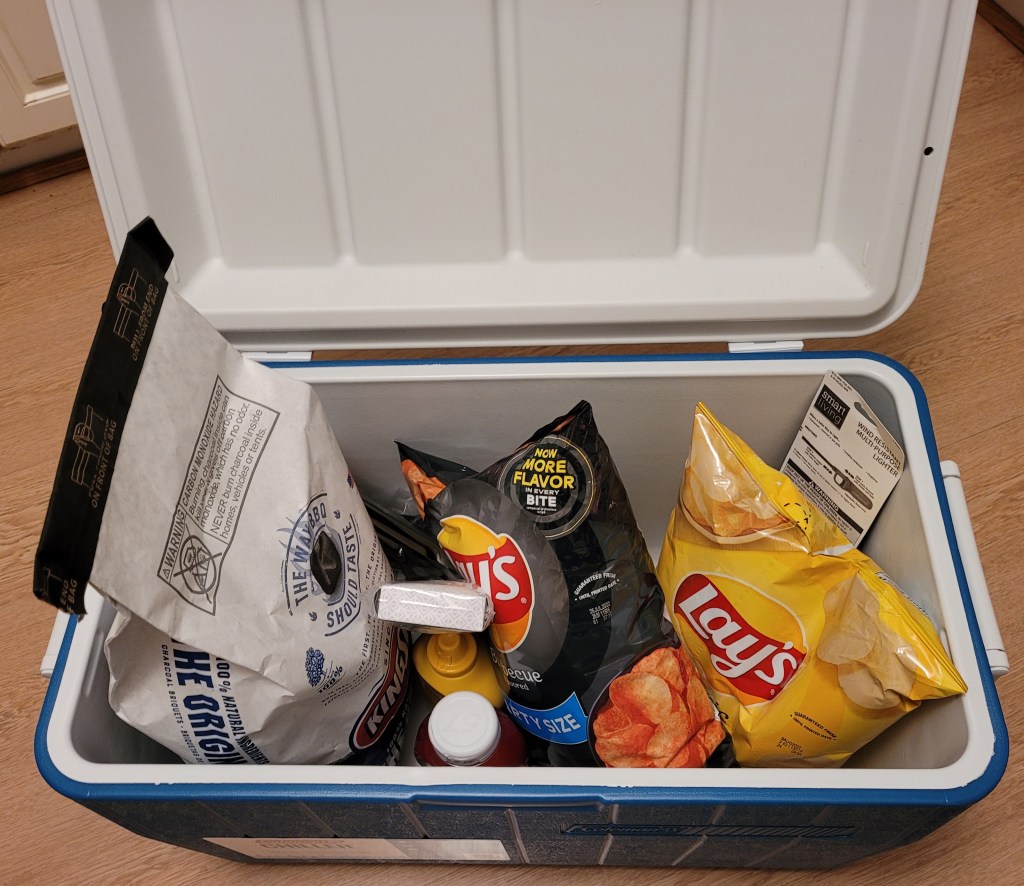 A Coleman cooler filled with grilling supplies and snacks