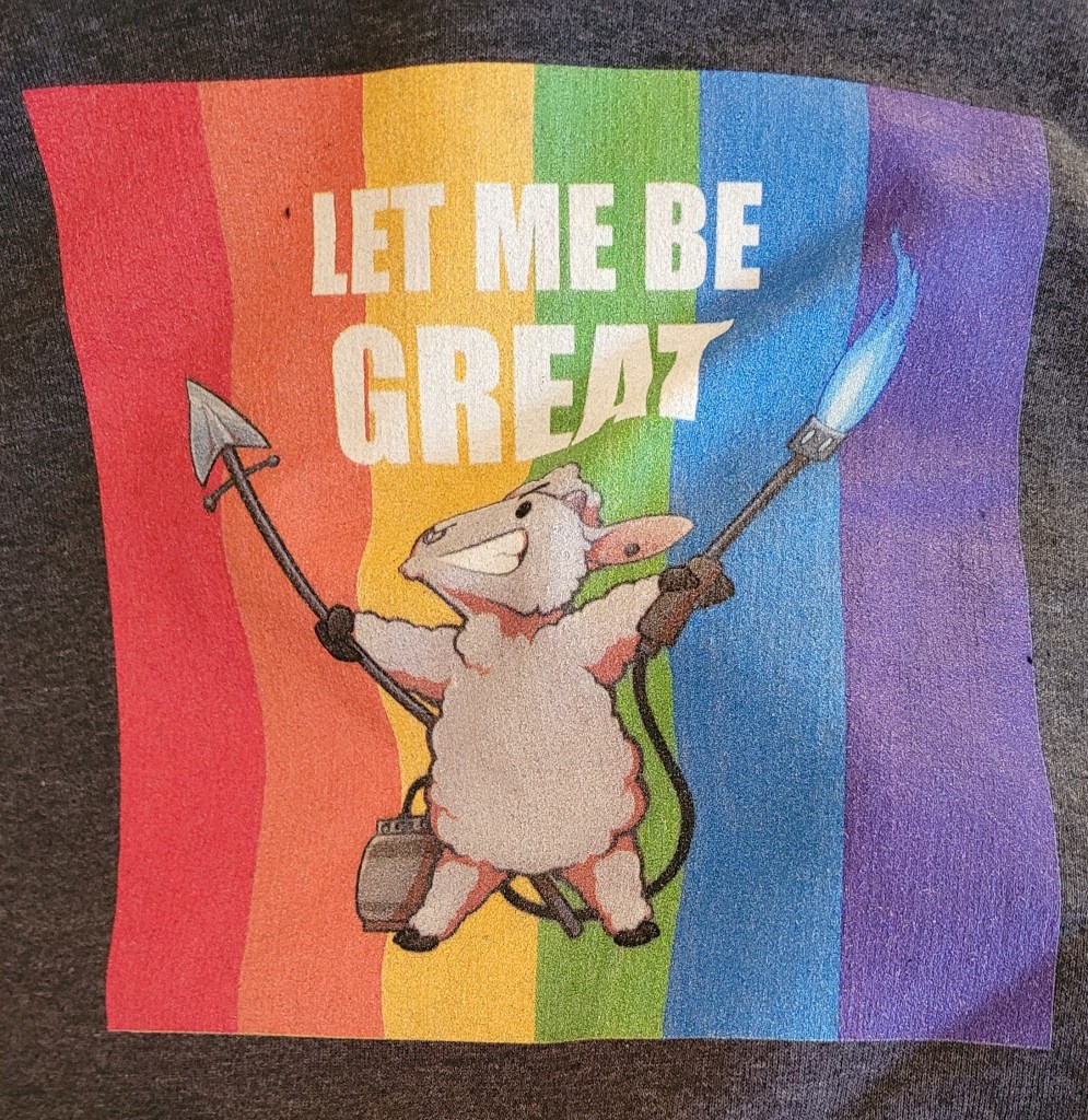 Hoodie with an illustrated sheep carrying a spear and a flamethrower on a rainbow background saying "Let Me Be Great"
