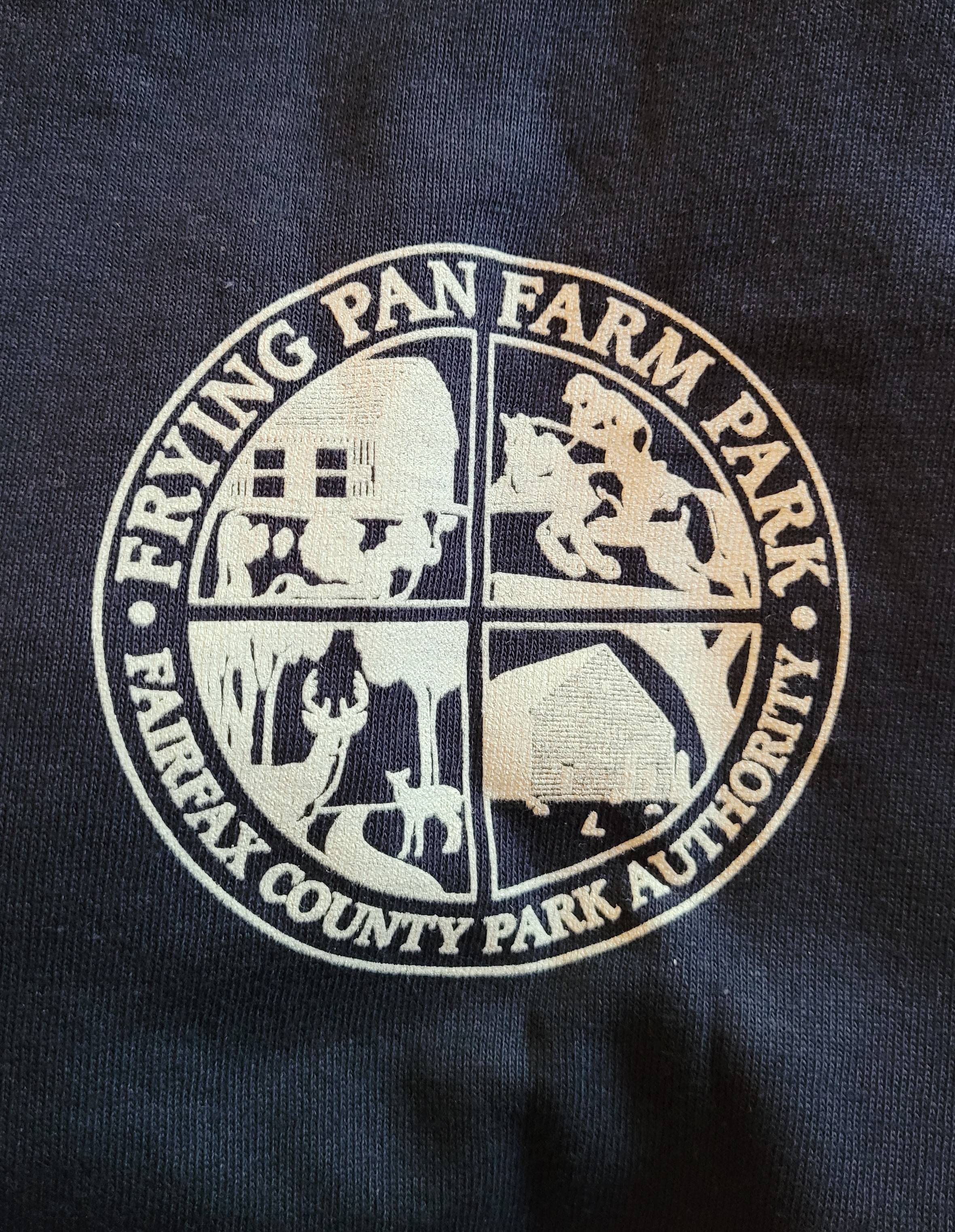 Detail of a t-shirt - the Frying Pan Farm Park logo showing illustrations of a barn, wildlife, and a horseback rider
