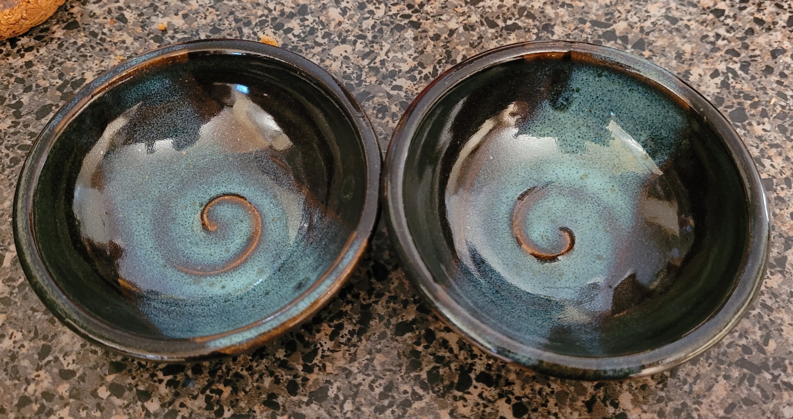 Two deep blue sauce dishes with a splash of lighter blue towards the center with a copper swirl in the middle