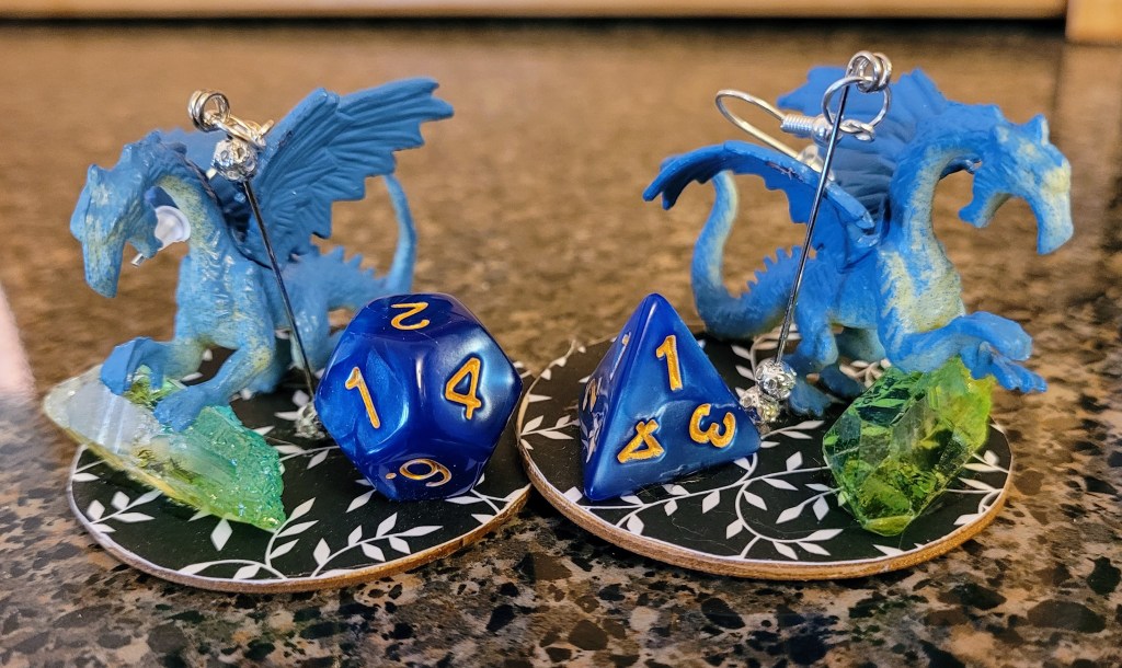 Earrings that have a dragon on a crystal and a DND dice on them.