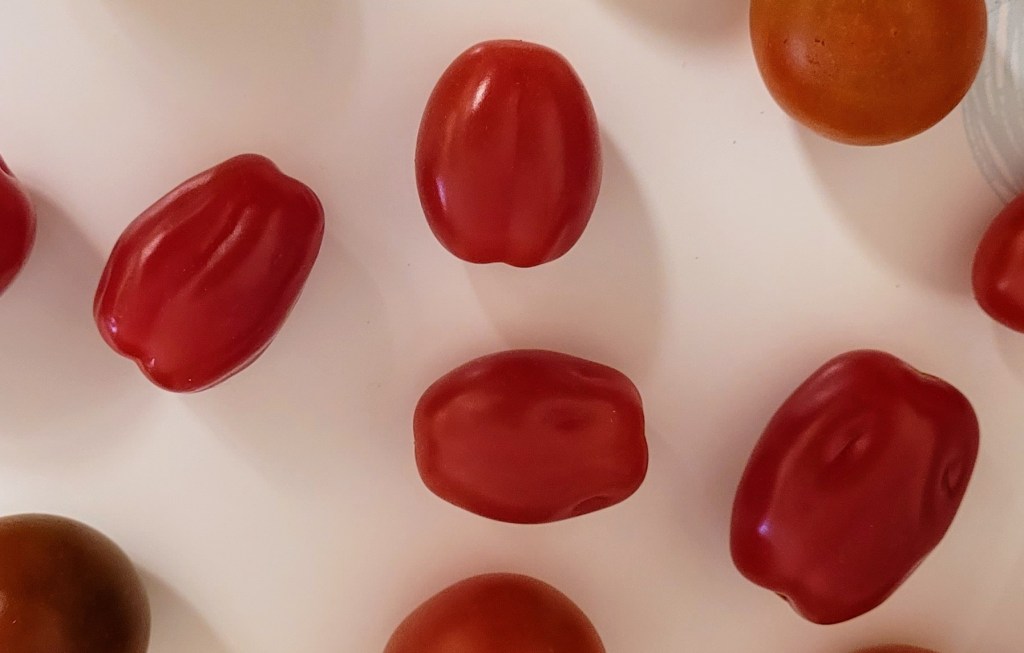 A plate with four small oval tomatoes with little divots in them - I think they are a type of grape tomato?