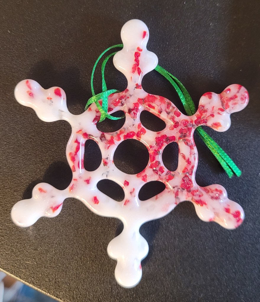 A glass snowflake ornament made from white glass with red bits scattered throughout that makes it look like it was made from a crushed candy cane