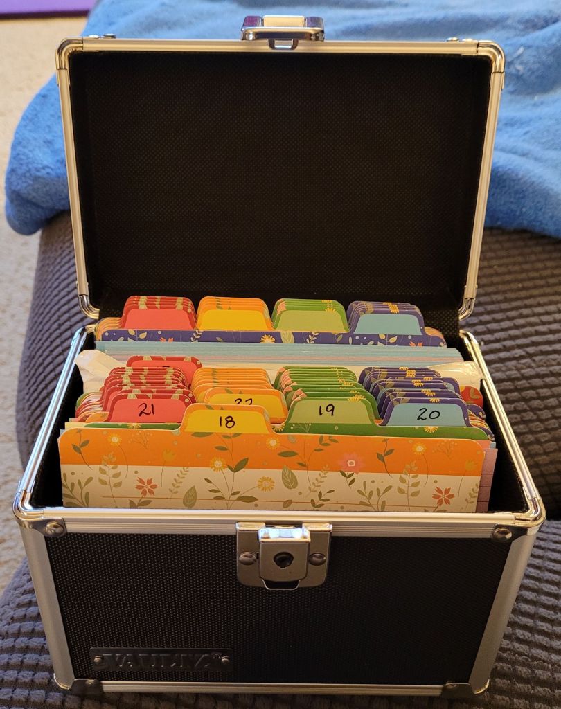 A black index card box with silver edges, opened to show multicolored dividers with the days of the month on them.