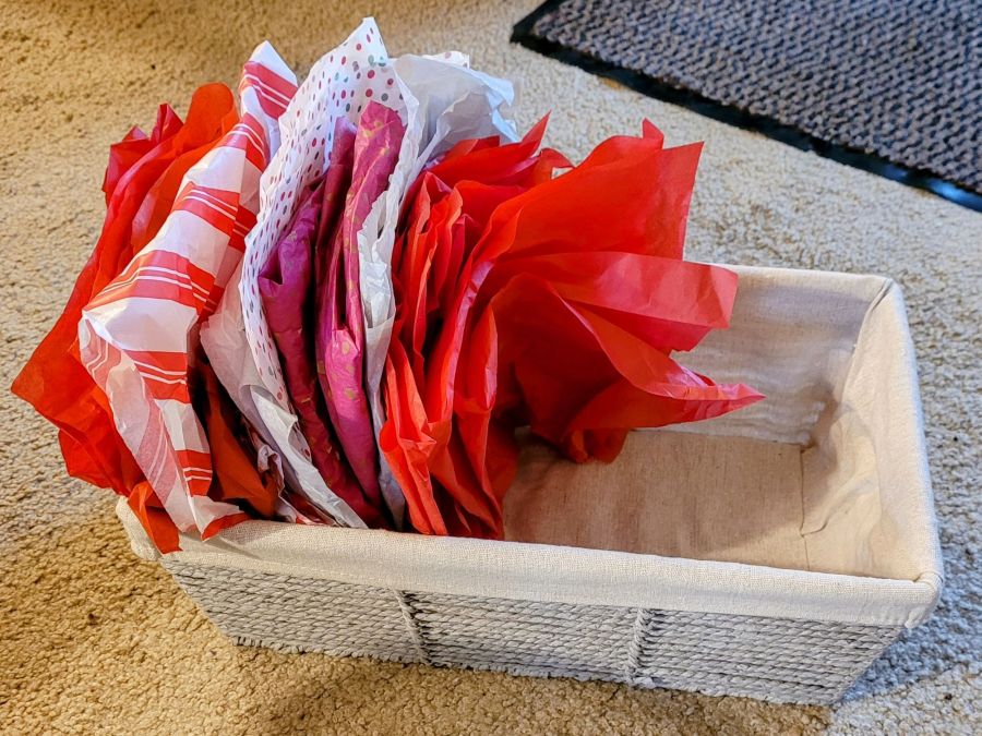 A beige fabric lined basket, half filled with folded Christmas themed sheets of tissue paper