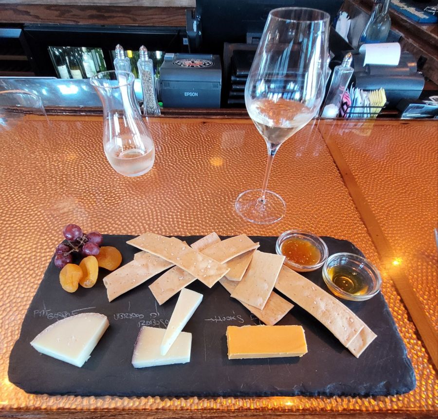 A slate platter with three kinds of cheese and crackers and jams and fruits