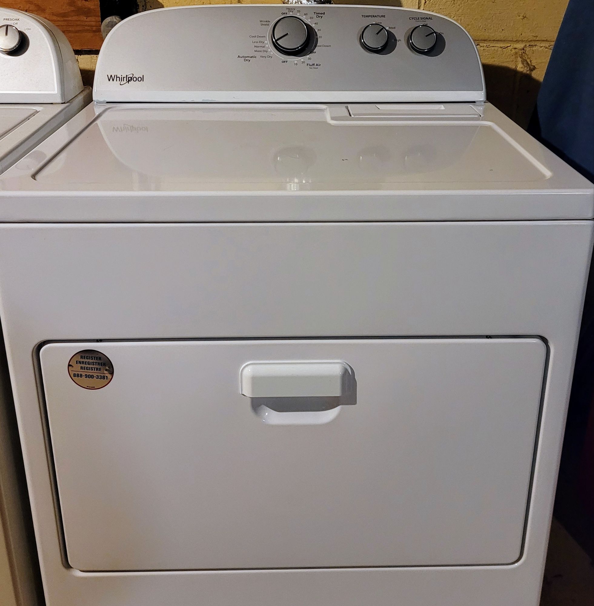 A white Whirlpool clothes dryer with a front drop down door and three knobs on top