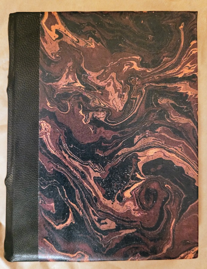 A small hand bound notebook with a marbled cover in various shades of brown.