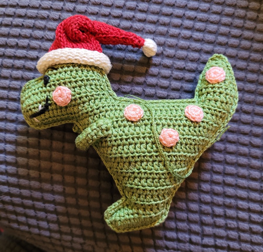 A crocheted dinosaur with a Santa hat