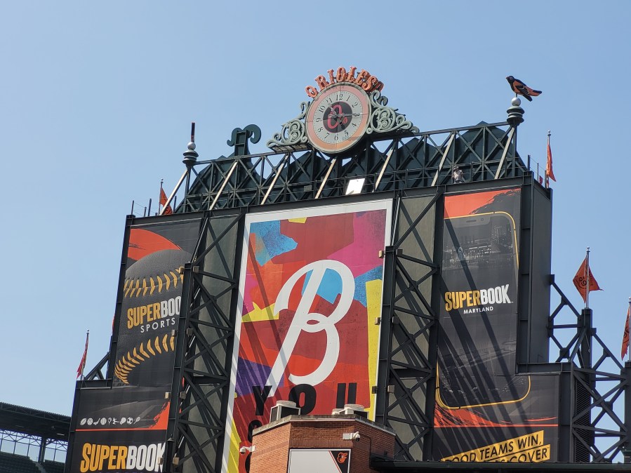 The back side of the scoreboard at Orioles Park, it has a large B with a multicolored mosaic background, and a clock at the top that says Orioles