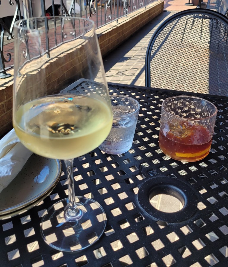 A glass of white wine in the foreground and a glass of bourbon in the background